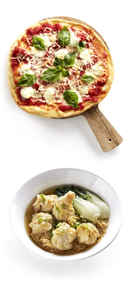 A margherita pizza with fresh basil on a wooden board sits above a bowl of wonton noodle soup with greens and dumplings, offering a delicious culinary experience reminiscent of the diverse dining options at River Rock Casino Resort.